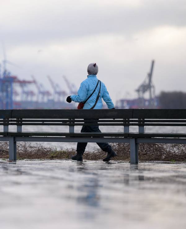 Eine Frau spaziert am 19. Februar 2022 an der Elbe bei Teufelsbrück vor der Hafenkulisse mit Containerbrücken.