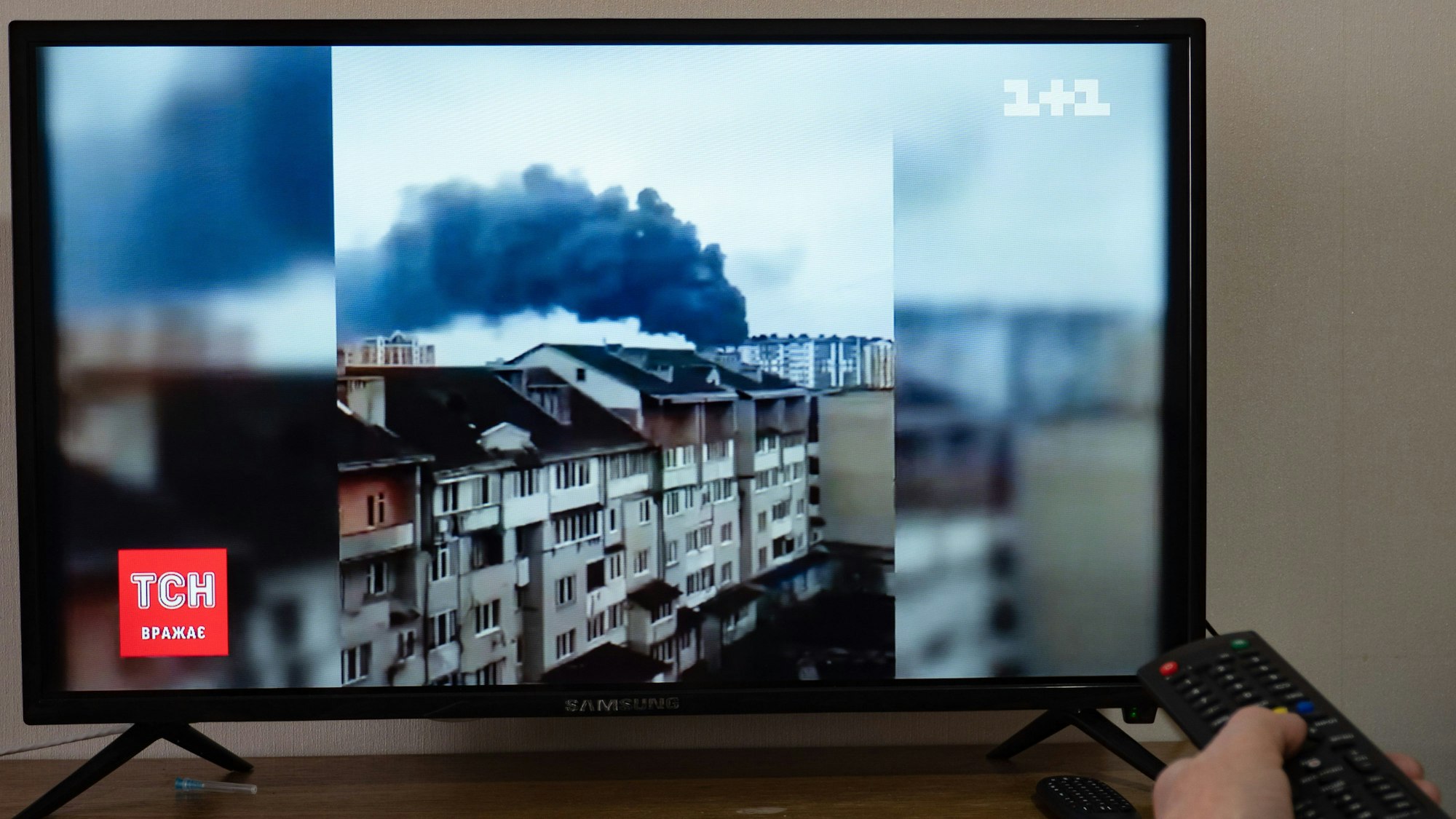 Eine Person bedient die Fernbedienung, während auf dem Fernsehbildschirm eine Nachrichtensendung, über einen russischen Angriff, zu sehen ist. Russische Truppen haben ihren erwarteten Angriff auf die Ukraine gestartet.