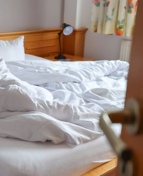 Auf dem Foto ist ein ungemachtes Bett in einem Hotelzimmer zu sehen.