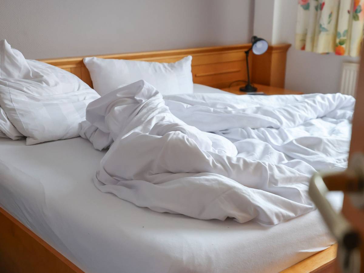 Auf dem Foto ist ein ungemachtes Bett in einem Hotelzimmer zu sehen.