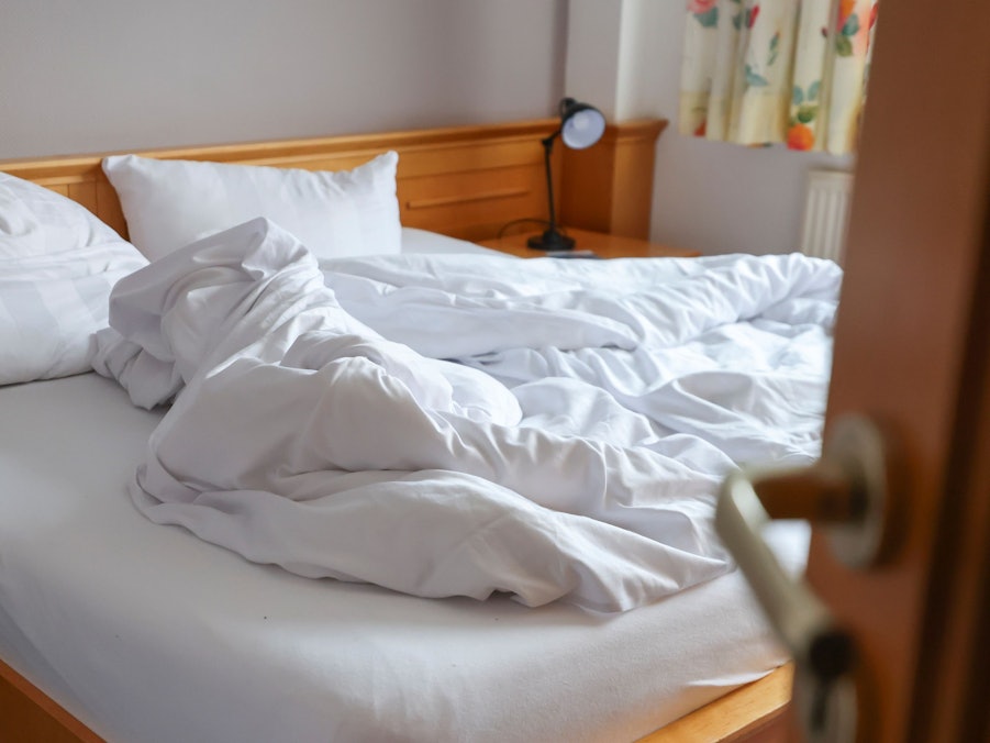 Auf dem Foto ist ein ungemachtes Bett in einem Hotelzimmer zu sehen.