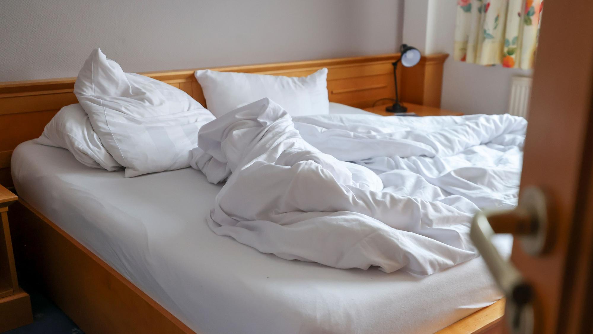 Auf dem Foto ist ein ungemachtes Bett in einem Hotelzimmer zu sehen.