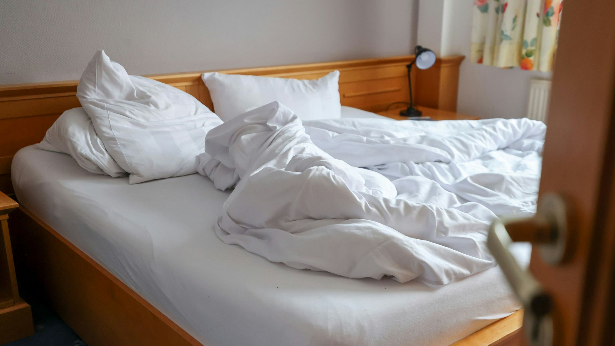 Auf dem Foto ist ein ungemachtes Bett in einem Hotelzimmer zu sehen.