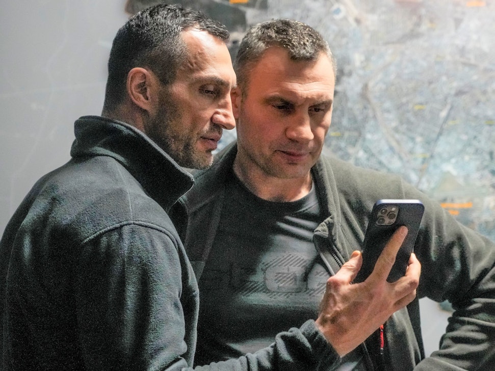 Vitali Klitschko (r), Bürgermeister von Kiew und ehemaliger Box-Profi, und sein Bruder Wladimir Klitschko, ebenfalls ehemaliger Box-Profi, schauen auf ein Smartphone im Rathaus in Kiew.