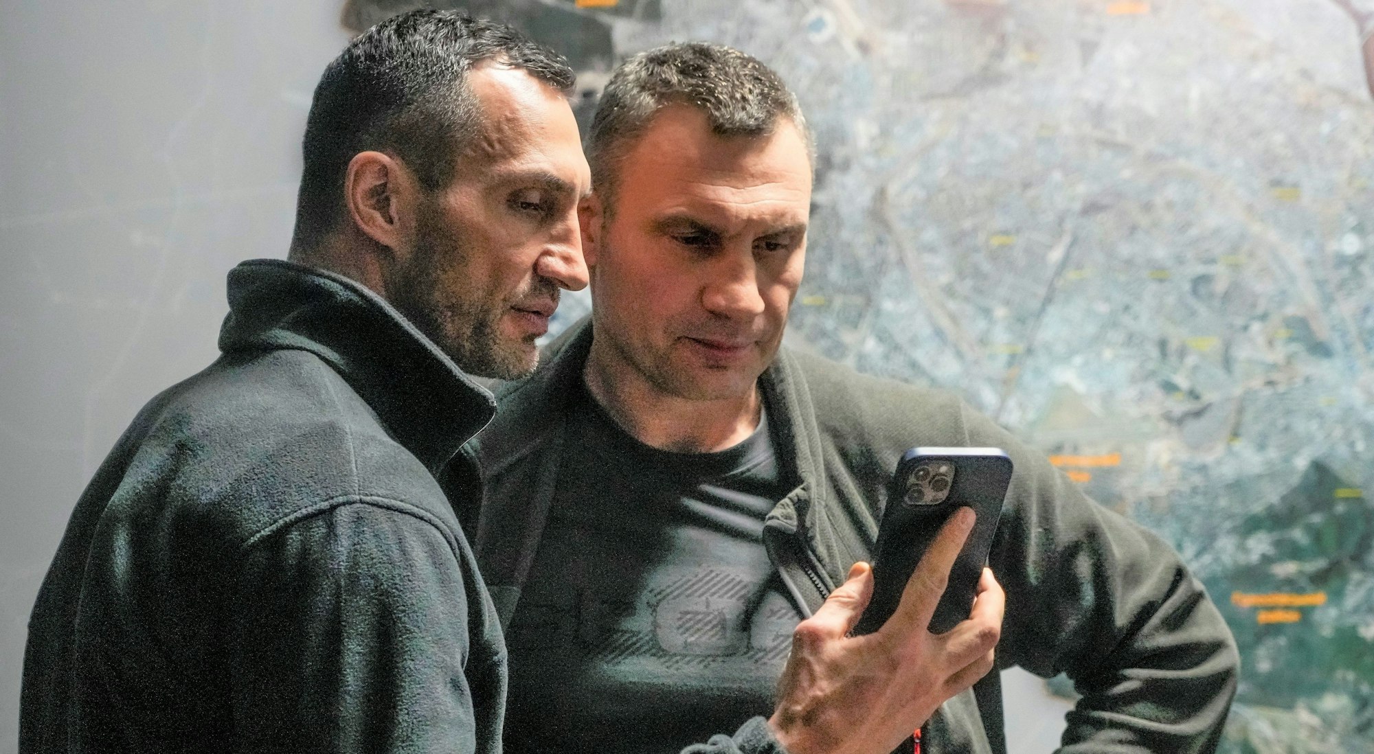 Vitali Klitschko (r), Bürgermeister von Kiew und ehemaliger Box-Profi, und sein Bruder Wladimir Klitschko, ebenfalls ehemaliger Box-Profi, schauen auf ein Smartphone im Rathaus in Kiew.