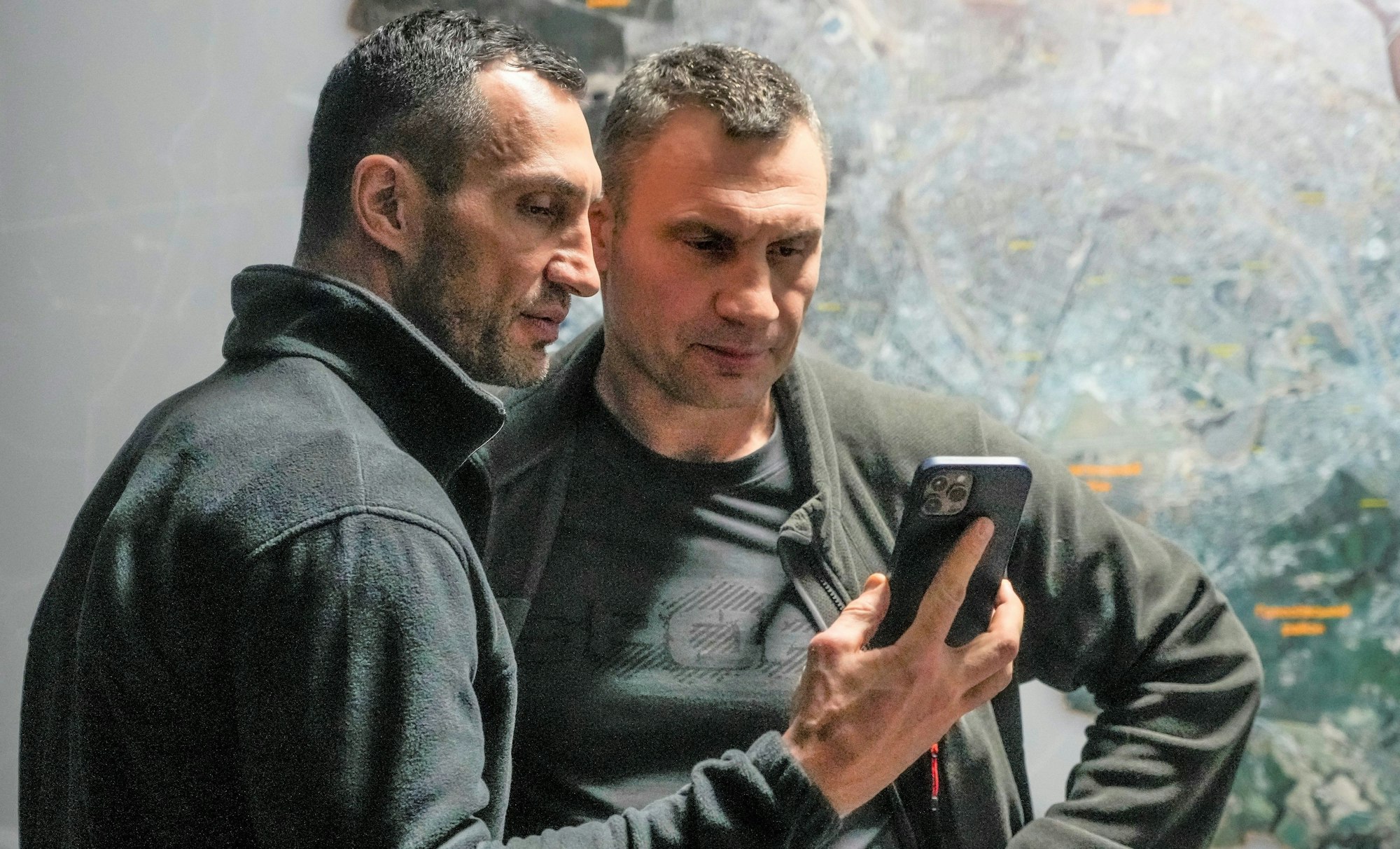 Vitali Klitschko (r), Bürgermeister von Kyjiw und ehemaliger Box-Profi, und sein Bruder Wladimir Klitschko, ebenfalls ehemaliger Box-Profi, schauen auf ein Smartphone im Rathaus in Kyjiw.