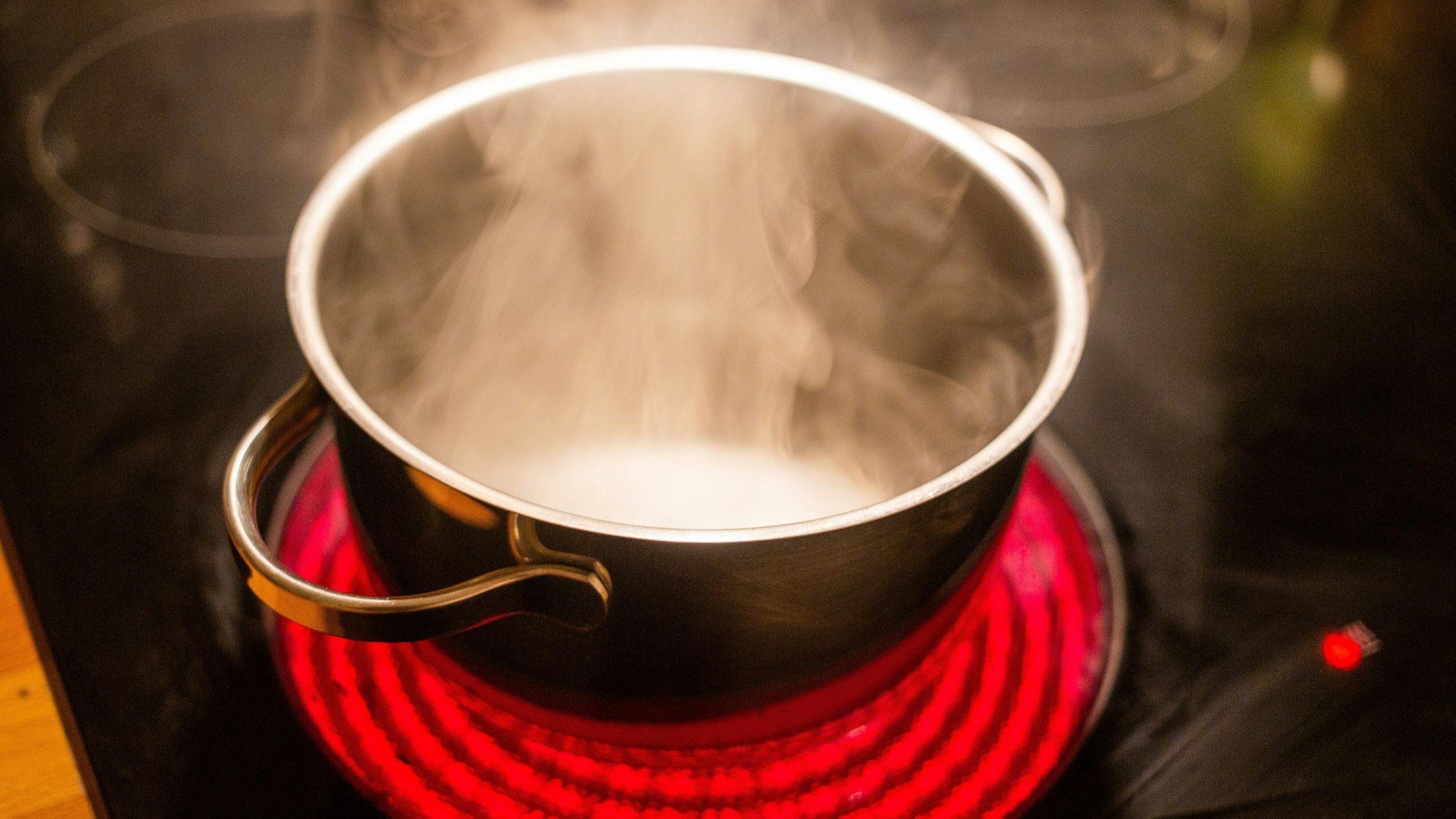 Ein Kochtopf mit kochendem Wasser steht auf einem Induktionskochfeld in einer Küche.