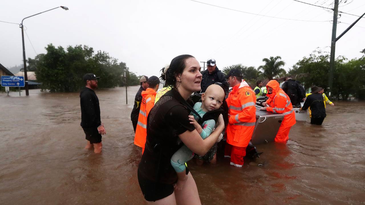 28.02.2022, Australien, Lismore: Eine Frau trägt ein Baby, während Menschen mit kleinen Booten durch das Hochwasser fahren. Sintflutartiger Regen hat die schweren Überschwemmungen im Osten Australiens weiter verschärft.
