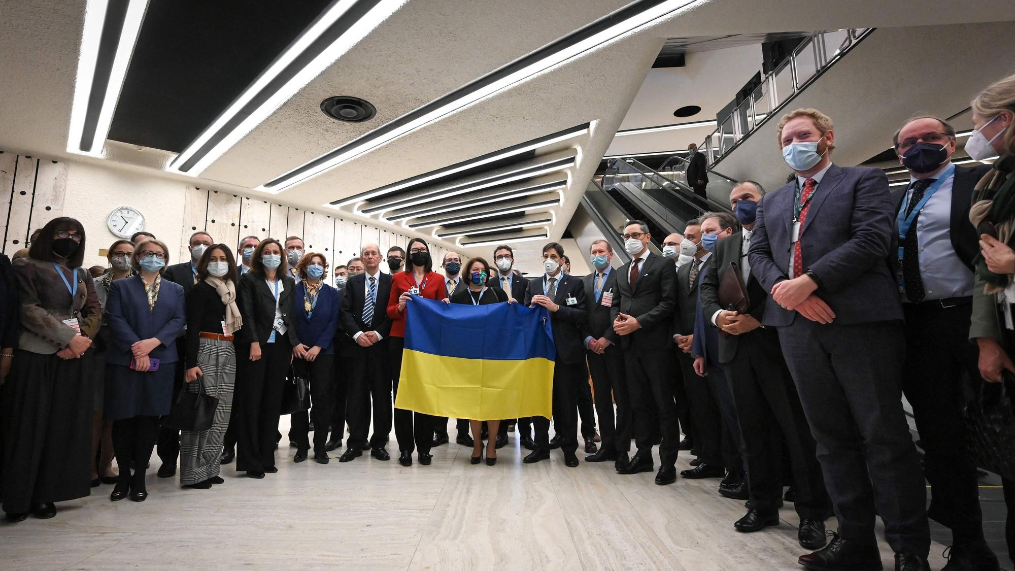 Diplomatinnen und Diplomaten versammeln sich neben der ukrainischen Botschafterin Jewjenija Filipenko (Mitte), die eine ukrainische Flagge hält. Während der russische Außenminister seine Rede hielt, verließen die meisten Botschafterinnen und Botschafter den Saal am Dienstag (1. März) in Genf.