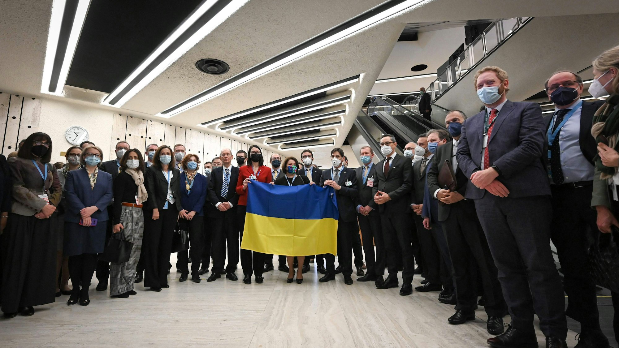 Diplomatinnen und Diplomaten versammeln sich neben der ukrainischen Botschafterin Jewjenija Filipenko (Mitte), die eine ukrainische Flagge hält. Während der russische Außenminister seine Rede hielt, verließen die meisten Botschafterinnen und Botschafter den Saal am Dienstag (1. März) in Genf.