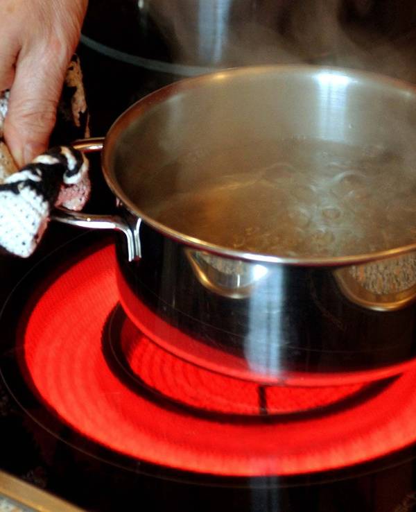 Ein Topf mit Wasser wird auf einen Elektroherd mit rot glühendem Ceran-Feld gestellt.