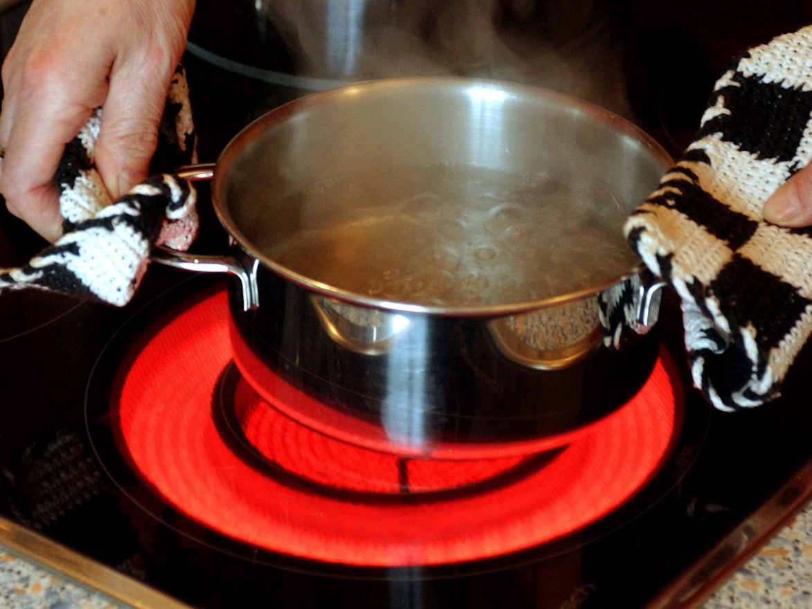 Ein Topf mit Wasser wird auf einen Elektroherd mit rot glühendem Ceran-Feld gestellt.