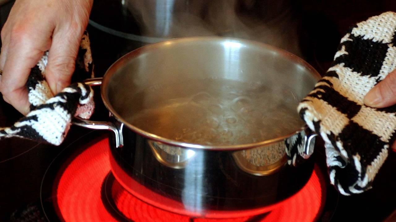 Ein Topf mit Wasser wird auf einen Elektroherd mit rot glühendem Ceran-Feld gestellt.