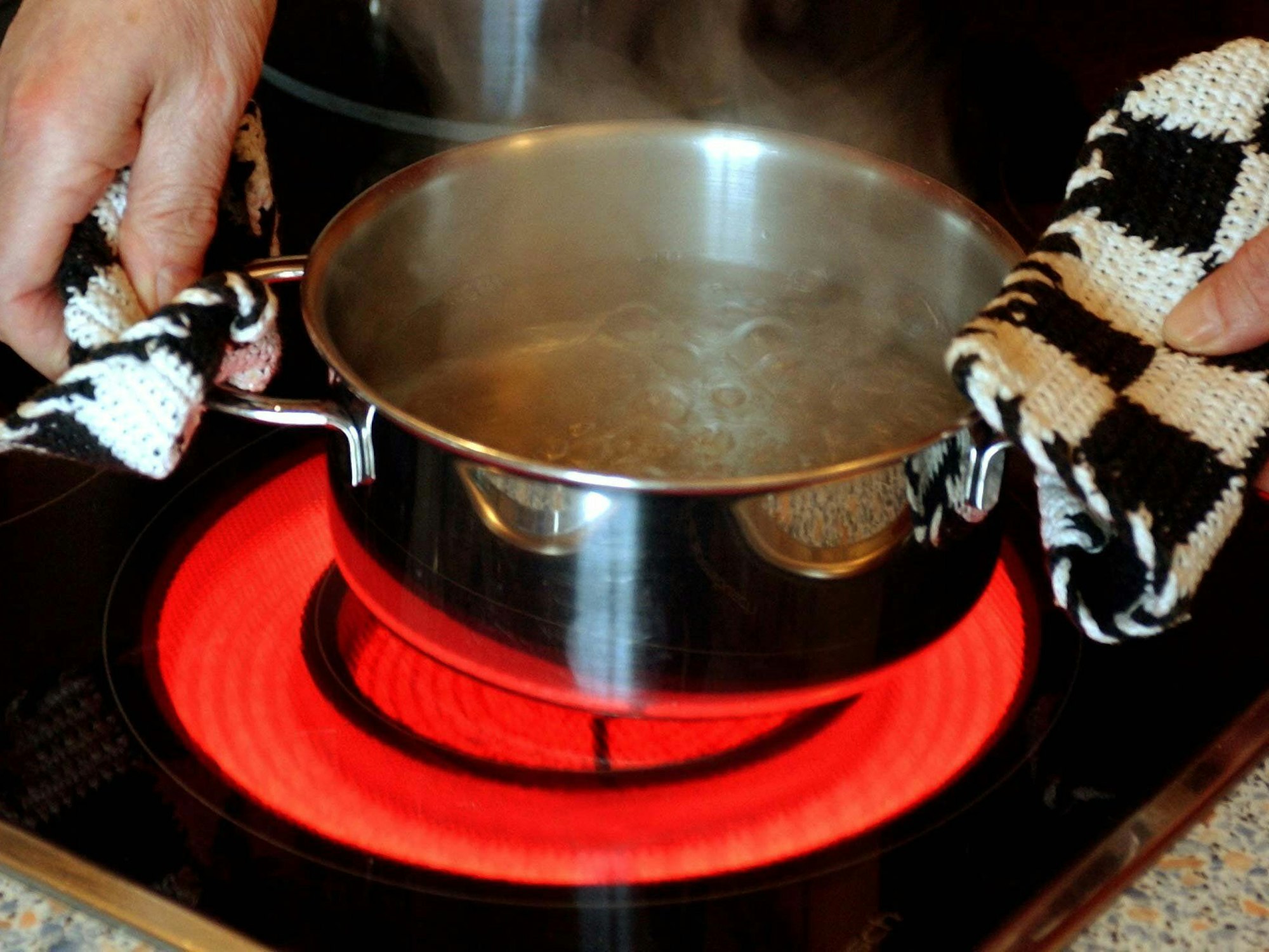 Ein Topf mit Wasser wird auf einen Elektroherd mit rot glühendem Ceran-Feld gestellt.