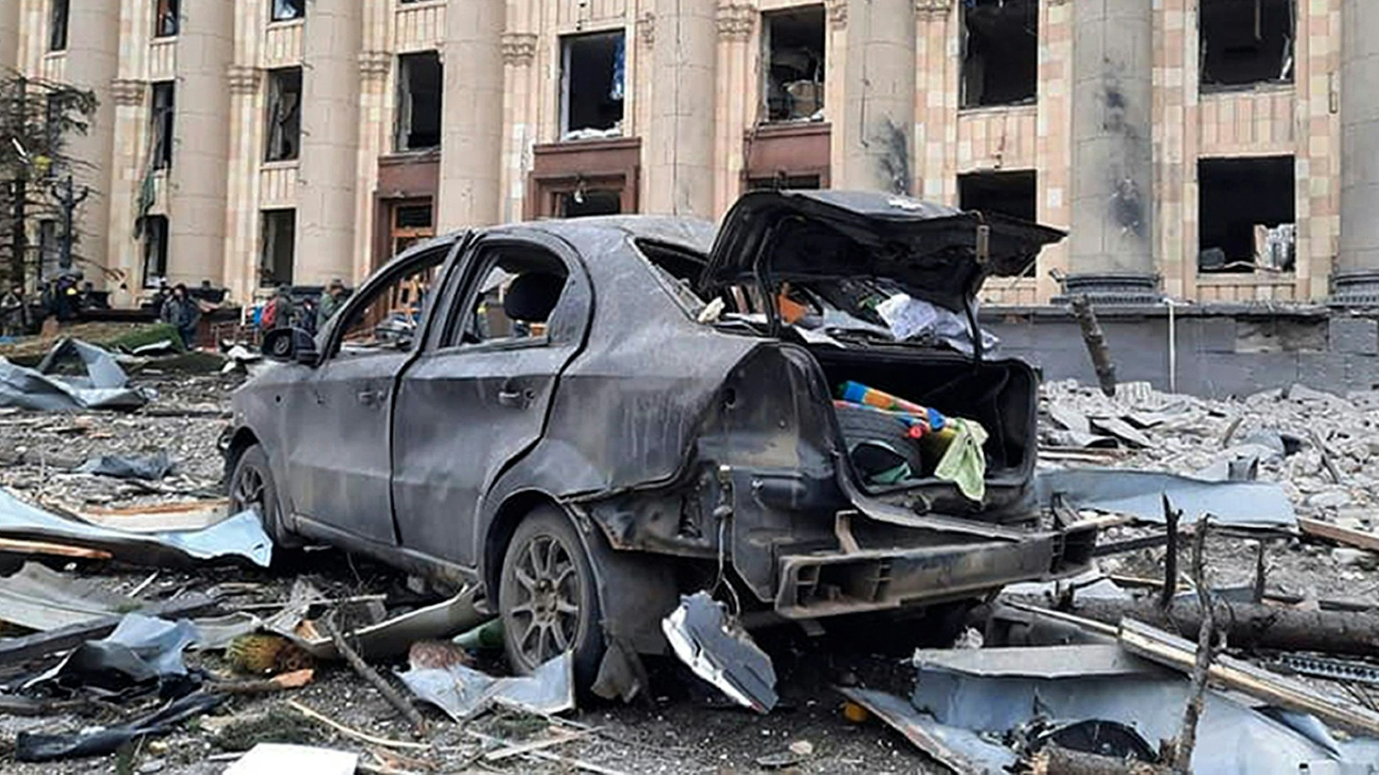 Ein zerstörtes Auto steht vor dem beschädigten Rathausgebäude von Charkiw