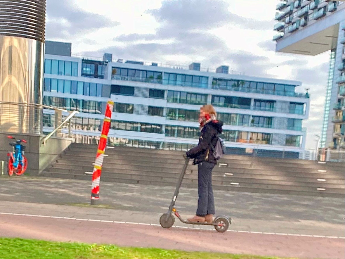 Ein Mast mitten auf dem Gehweg am Rheinauhafen in Köln, fotografiert vor wenigen Tagen. Eine Person fährt mit einem Roller daran vorbei.