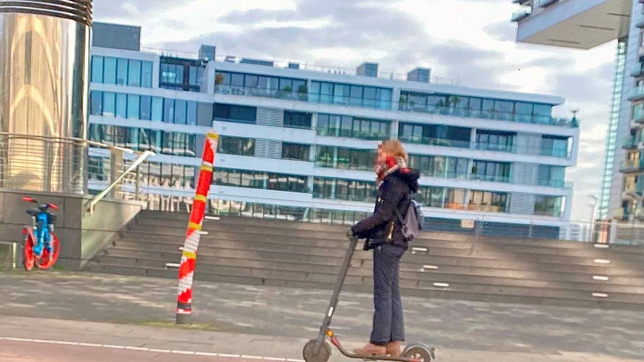 Ein Mast mitten auf dem Gehweg am Rheinauhafen in Köln, fotografiert vor wenigen Tagen. Eine Person fährt mit einem Roller daran vorbei.