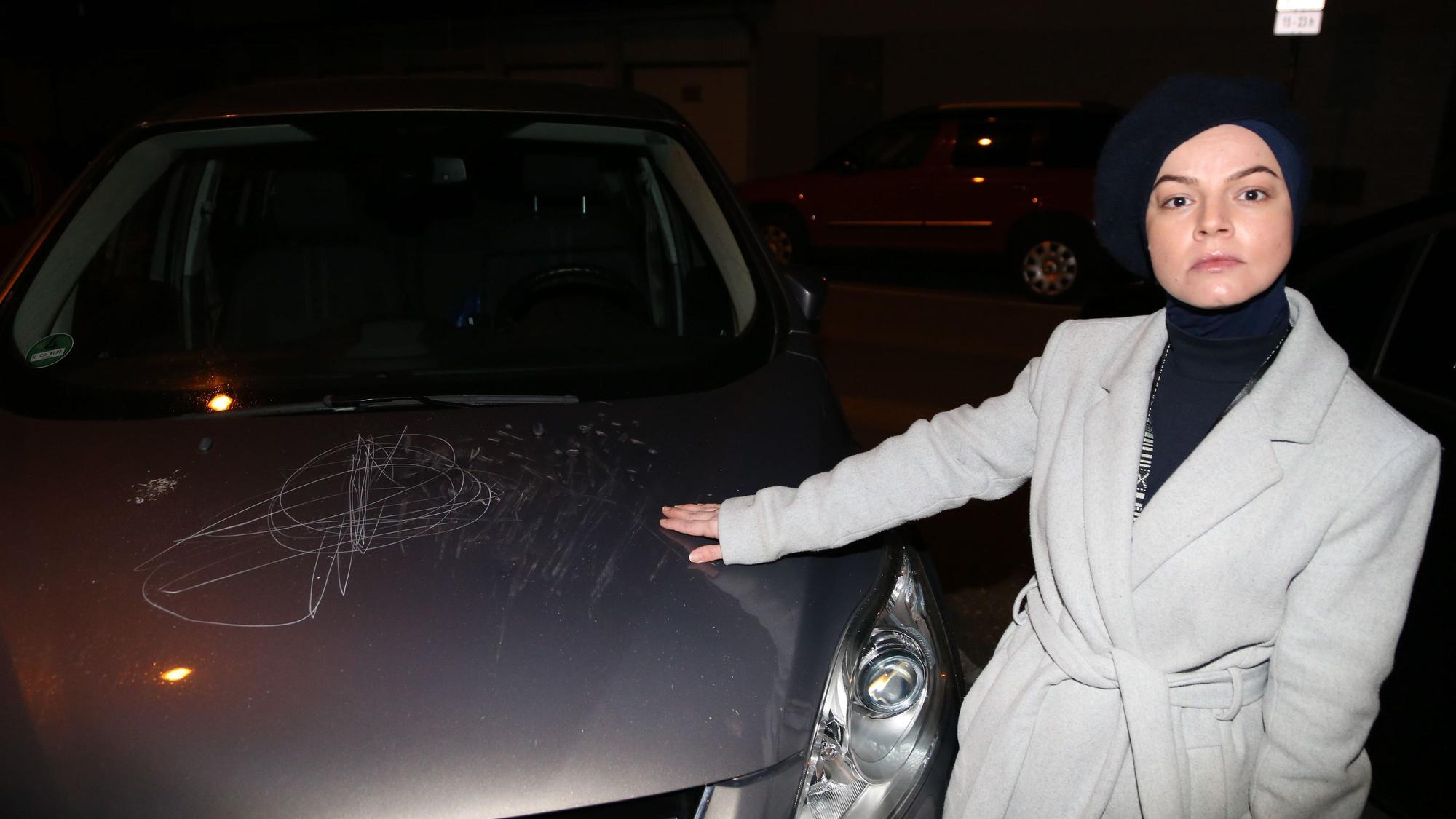 Eine Frau steht neben ihrem Auto, das zerkratzt wurde.