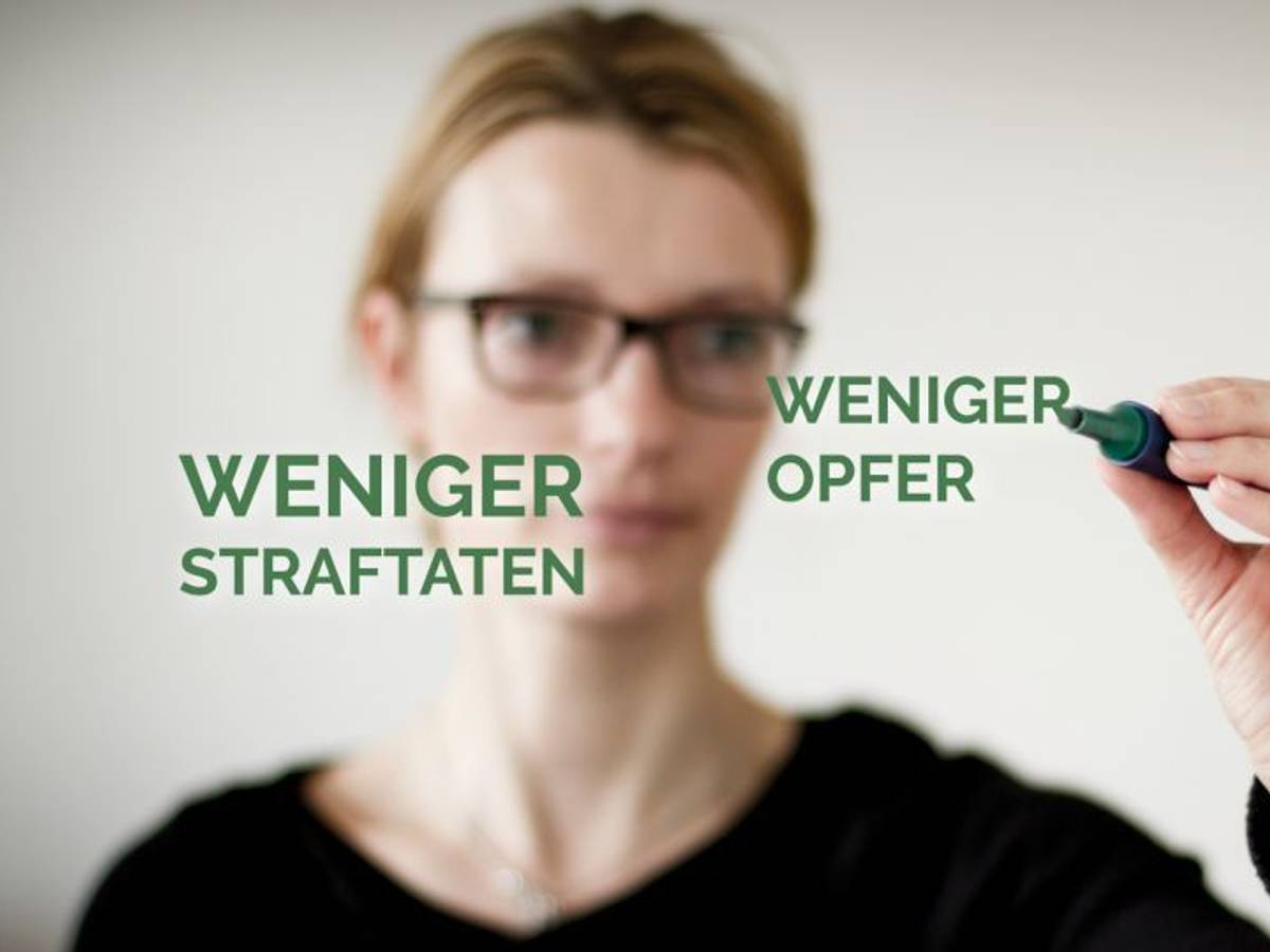 Eine Frau schreibt mit einem Stift auf eine Glasscheibe, auf der die Begriffe „Weniger Straftaten“ und „Weniger Opfer“ zu sehen sind.