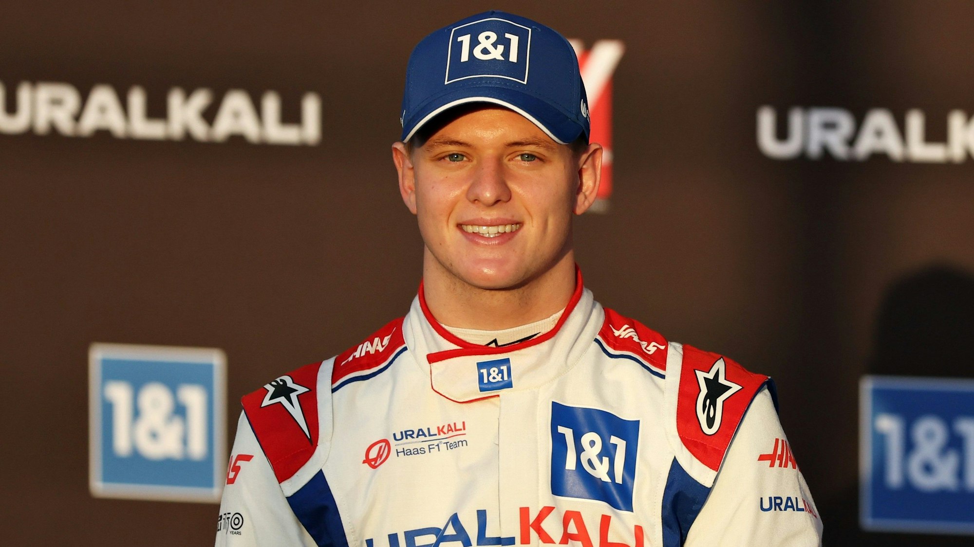 Mick Schumacher steht bei einem Foto-Shooting der Formel 1 vor einer Werbe-Wand.