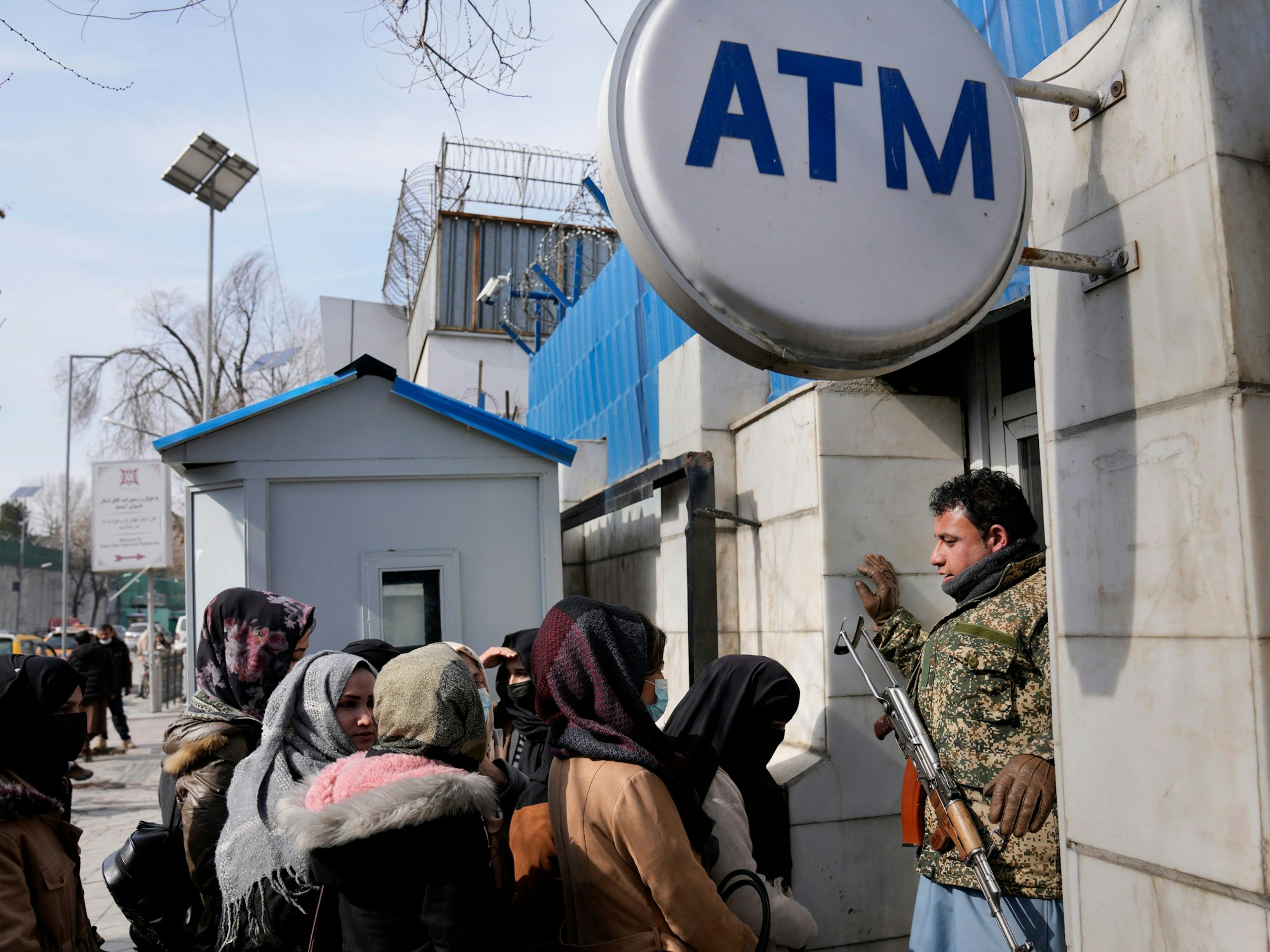 Ein afghanischer Sicherheitsbeamter mit einem AK-47 Gewehr steht vor einer Gruppe Frauen, die an einem Geldautomaten anstehen.