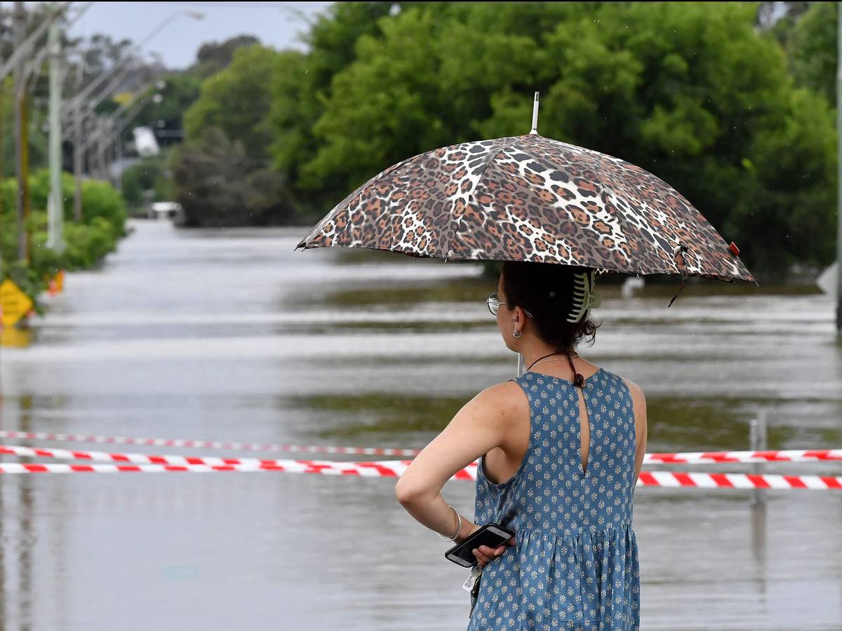 Eine Frau steht mit Schirm vor den überfluteten Straßen von Sydney. Heftige Unwetter suchen die australische Metropole heim.