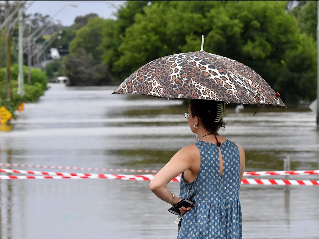 Eine Frau steht mit Schirm vor den überfluteten Straßen von Sydney. Heftige Unwetter suchen die australische Metropole heim.