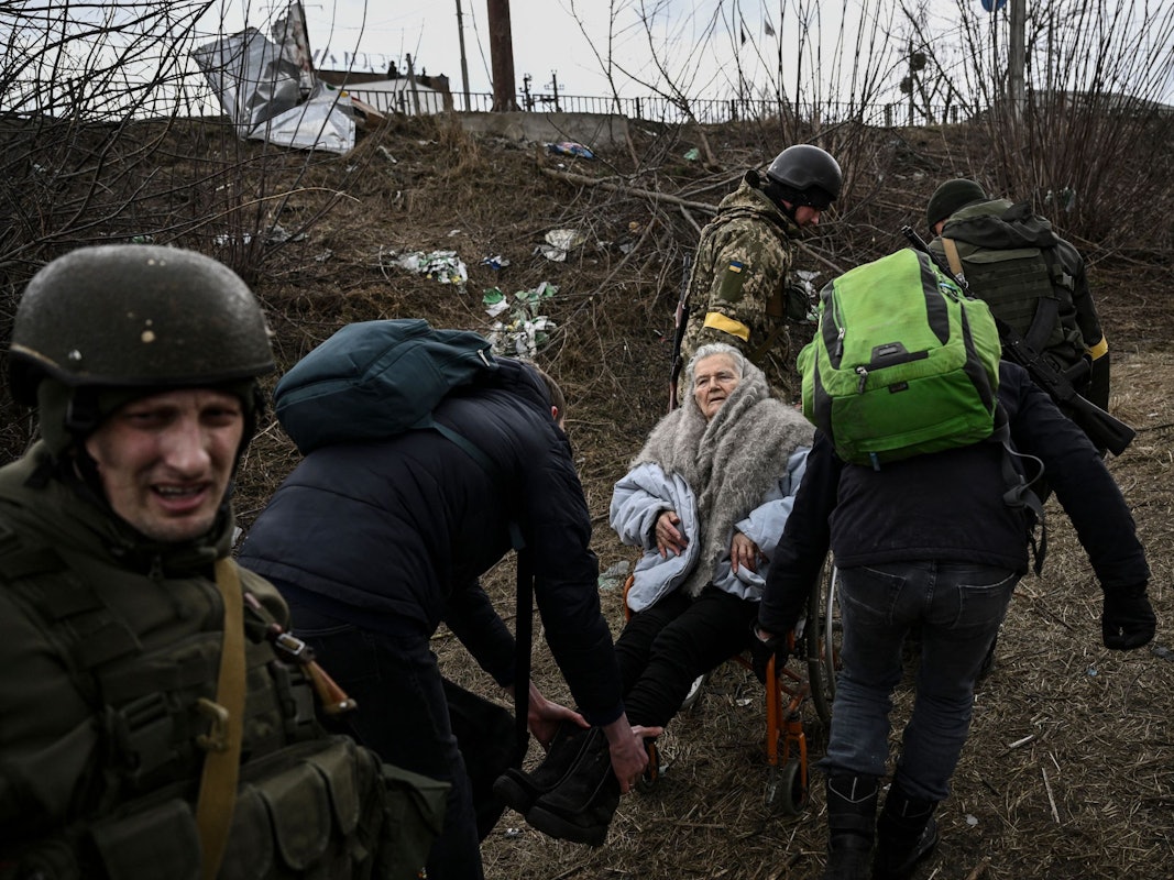 Menschen helfen einer älteren Frau im Rollstuhl, als sie am 7. März aus der Stadt Irpin westlich von Kiew fliehen. Die Lage in der Ukraine spitzt sich weiter zu.