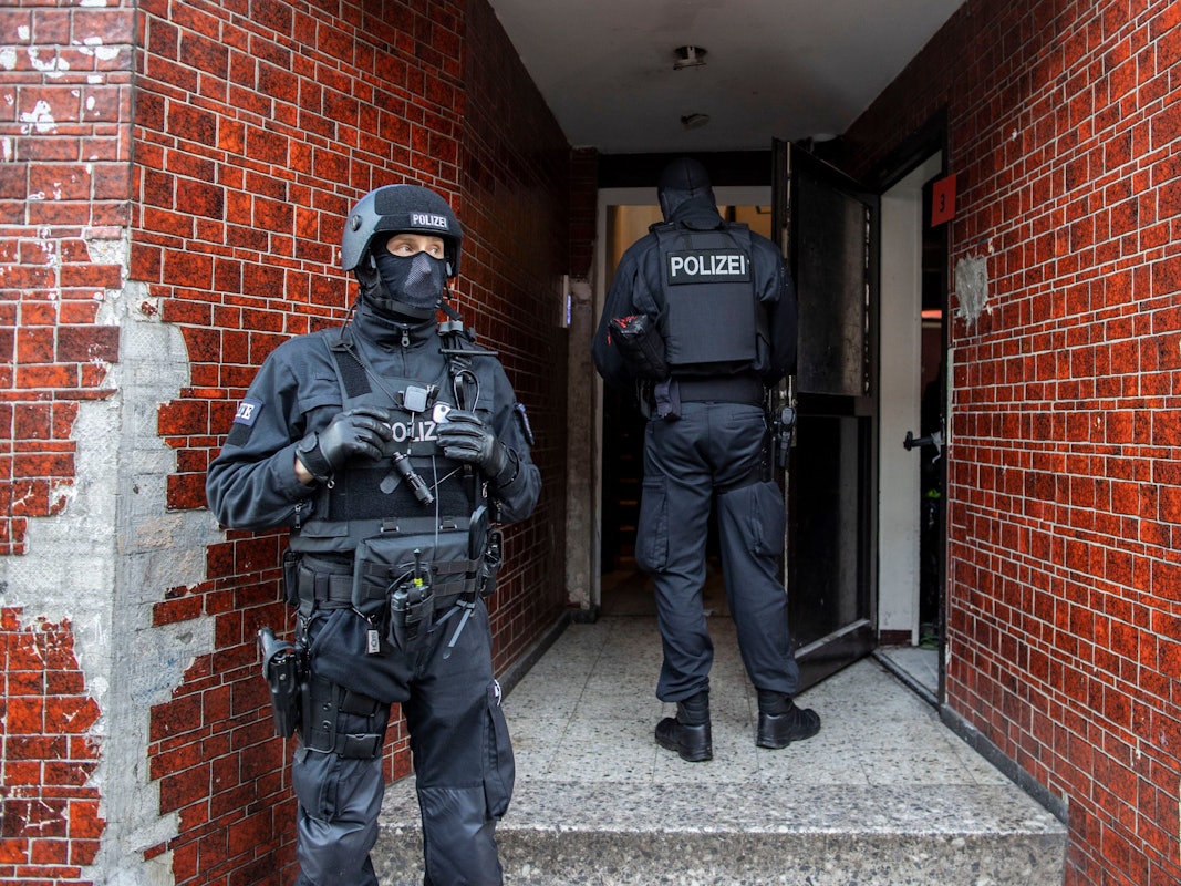 Polizisten stehen bei einer Razzia in einem Hauseingang.