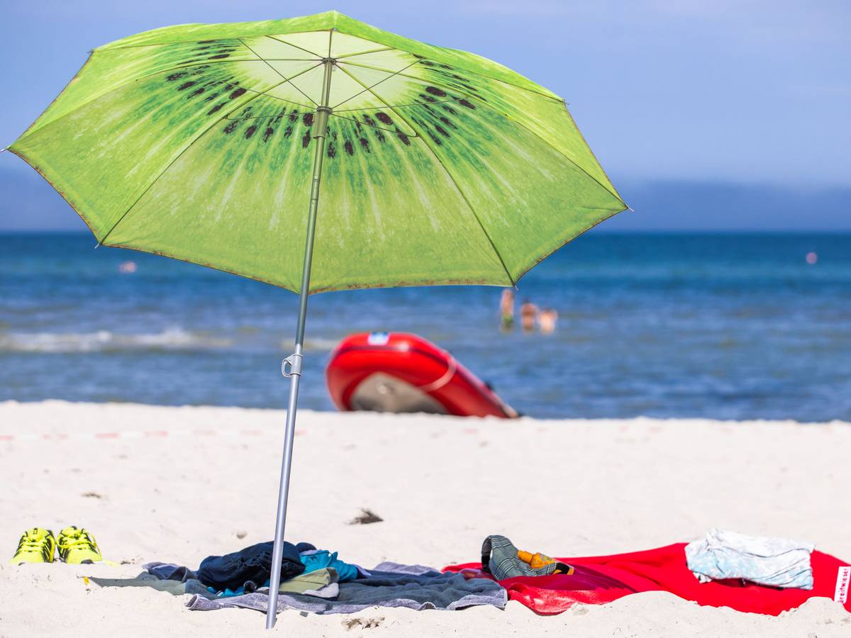 Ein grüner Sonnenschirm steht am Strand an der Ostseeküste.