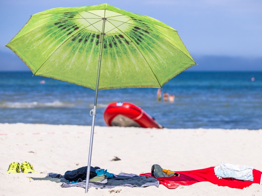 Ein grüner Sonnenschirm steht am Strand an der Ostseeküste.