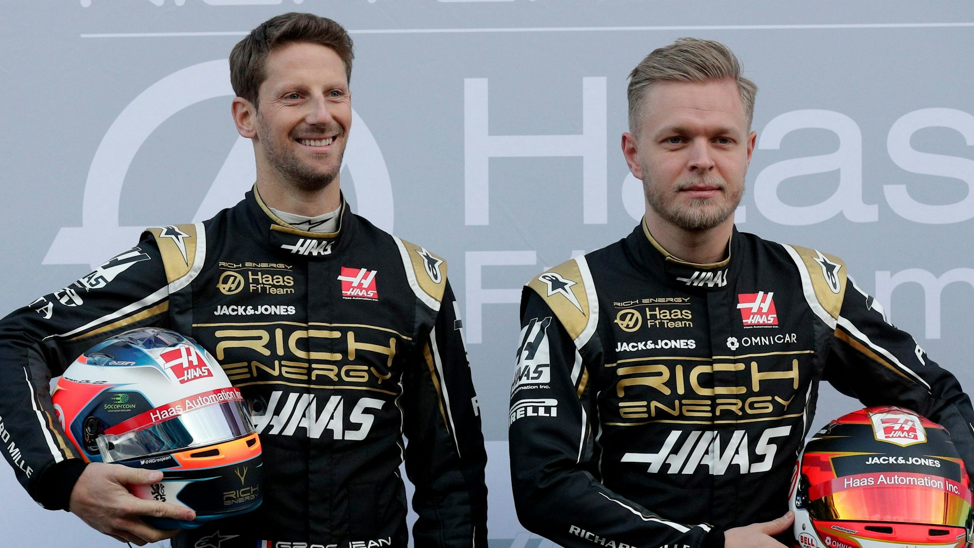 18.02.2019, Spanien, Montmelo: Die Fahrer Kevin Magnussen aus Dänemark (r) und Romain Grosjean aus Frankreich lassen sich mit dem neuen Haas F1-Auto während einer Präsentation auf der Rennstrecke Barcelona Catalunya in Montmelo, außerhalb von Barcelona fotografieren.