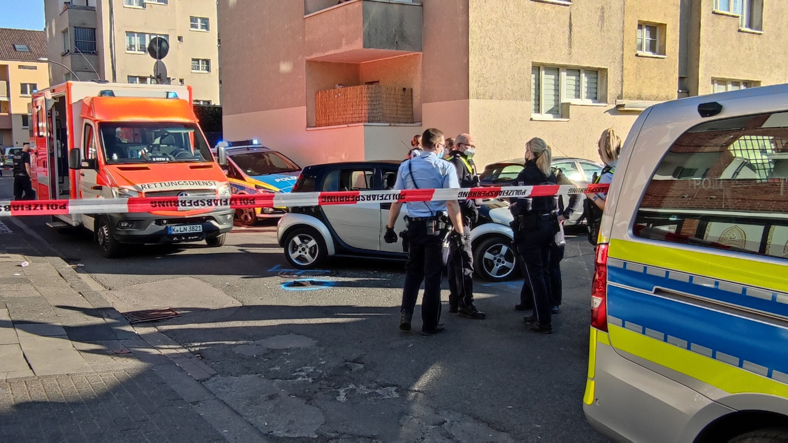 Einsatzkräfte von Polizei und Rettungsdienst stehen auf einer Straße, die mit Flatterband abgesperrt ist.