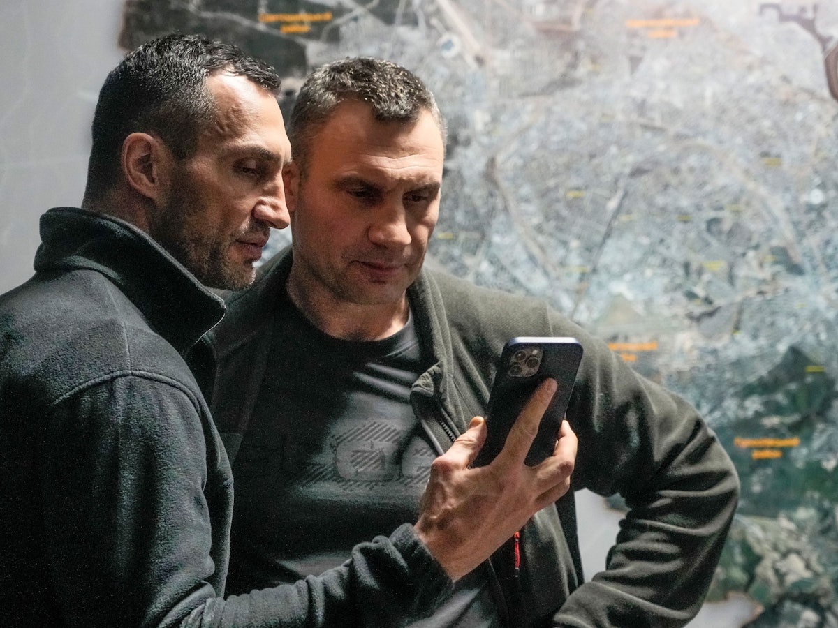 Vitali Klitschko (r), Bürgermeister von Kiew und ehemaliger Box-Profi, und sein Bruder Wladimir Klitschko, ebenfalls ehemaliger Box-Profi, schauen auf ein Smartphone im Rathaus in Kiew.