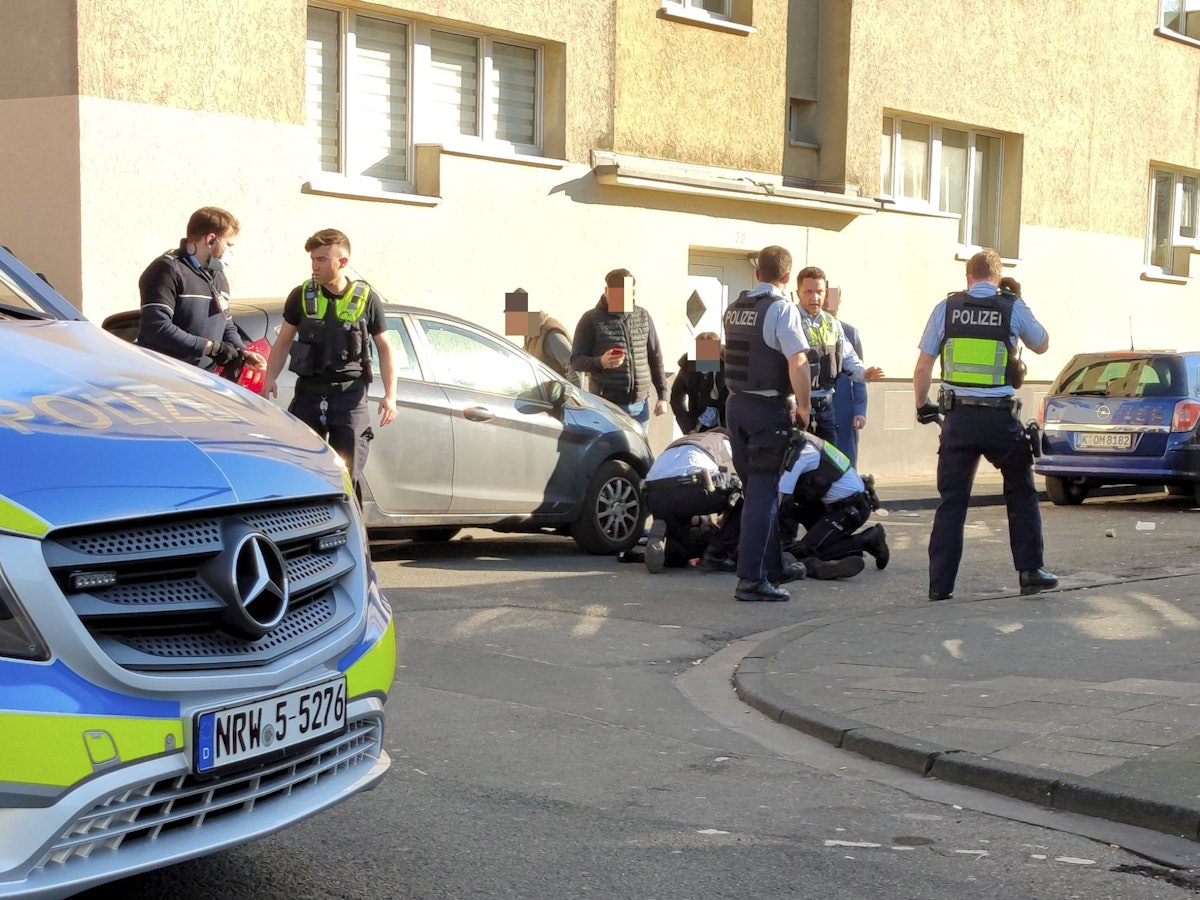 Einsatzkräfte und Passanten stehen oder knien neben einem Verletzten, der auf dem Boden liegt.
