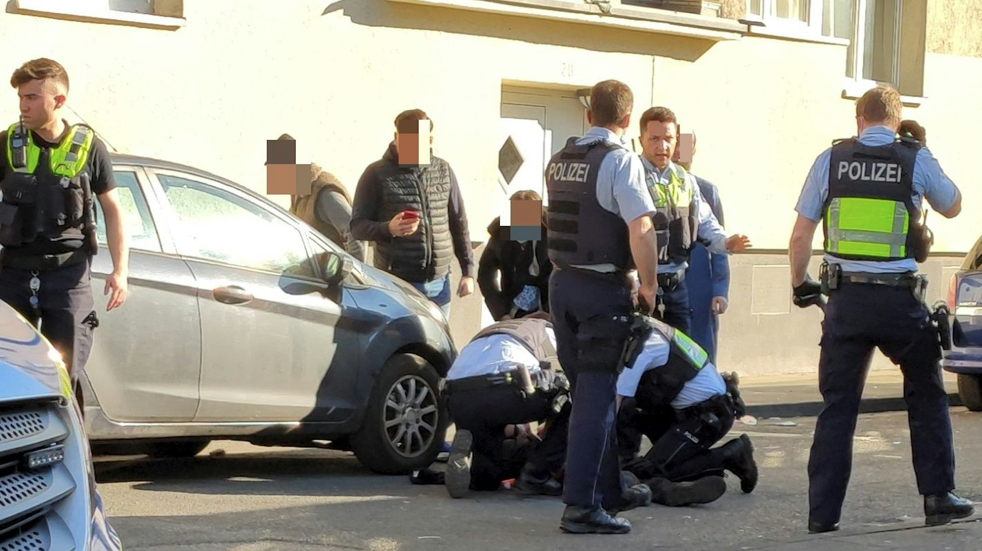Einsatzkräfte und Passanten stehen oder knien neben einem Verletzten, der auf dem Boden liegt.