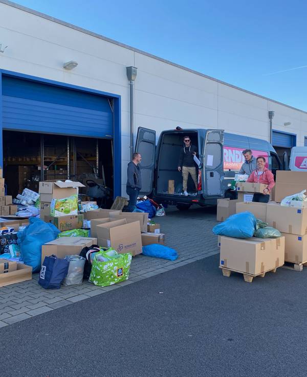 Junge Kölner vor einer Lagerhalle, die mit Umzugskartons voll mit Sachspenden gefüllt ist