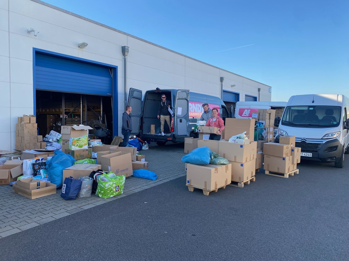 Junge Kölner vor einer Lagerhalle, die mit Umzugskartons voll mit Sachspenden gefüllt ist