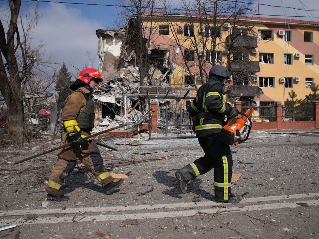 Feuerwehrleute gehen an einem durch Beschuss beschädigten Gebäude in Mariupol vorbei