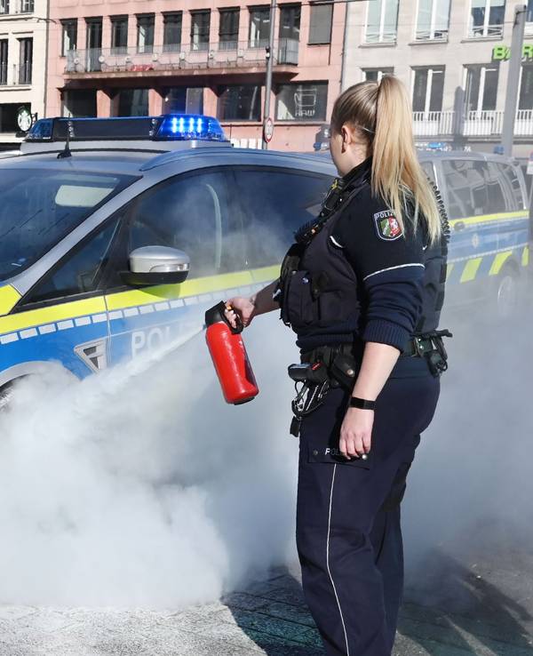 Eine Polizistin zielt mit einem Feuerlöscher auf das Rad eines Streifenwagens..