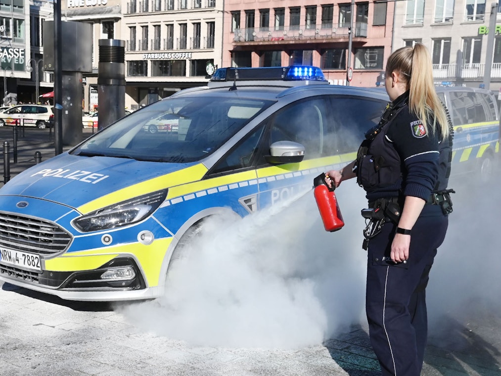 Eine Polizistin zielt mit einem Feuerlöscher auf das Rad eines Streifenwagens..