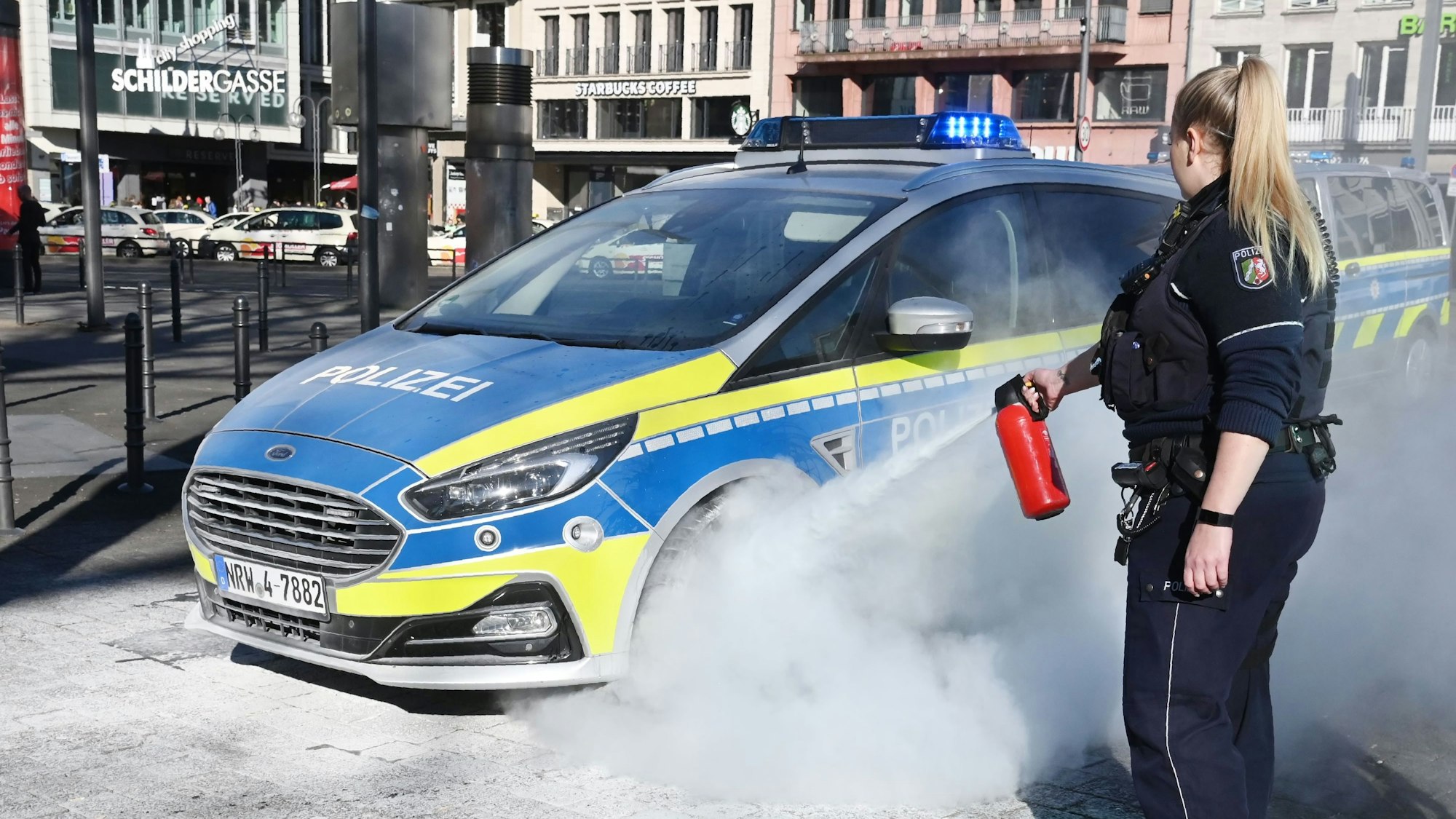 Eine Polizistin zielt mit einem Feuerlöscher auf das Rad eines Streifenwagens..