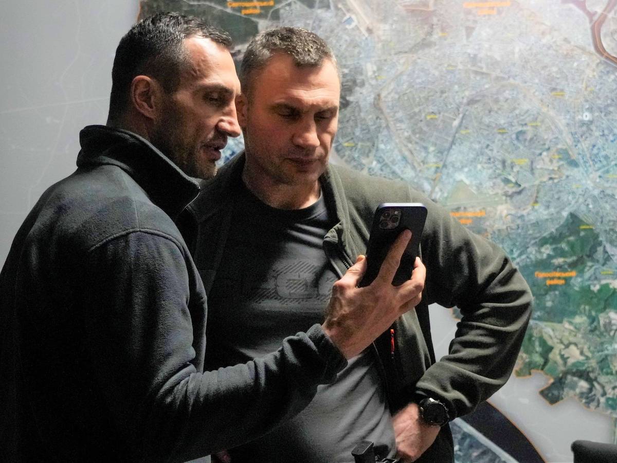 Wladimir (l.) und Vitali Klitschko schauen in einem Büro in Kiew auf ein Handy.