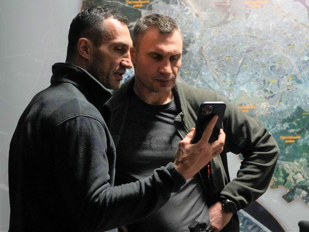 Wladimir (l.) und Vitali Klitschko schauen in einem Büro in Kiew auf ein Handy.