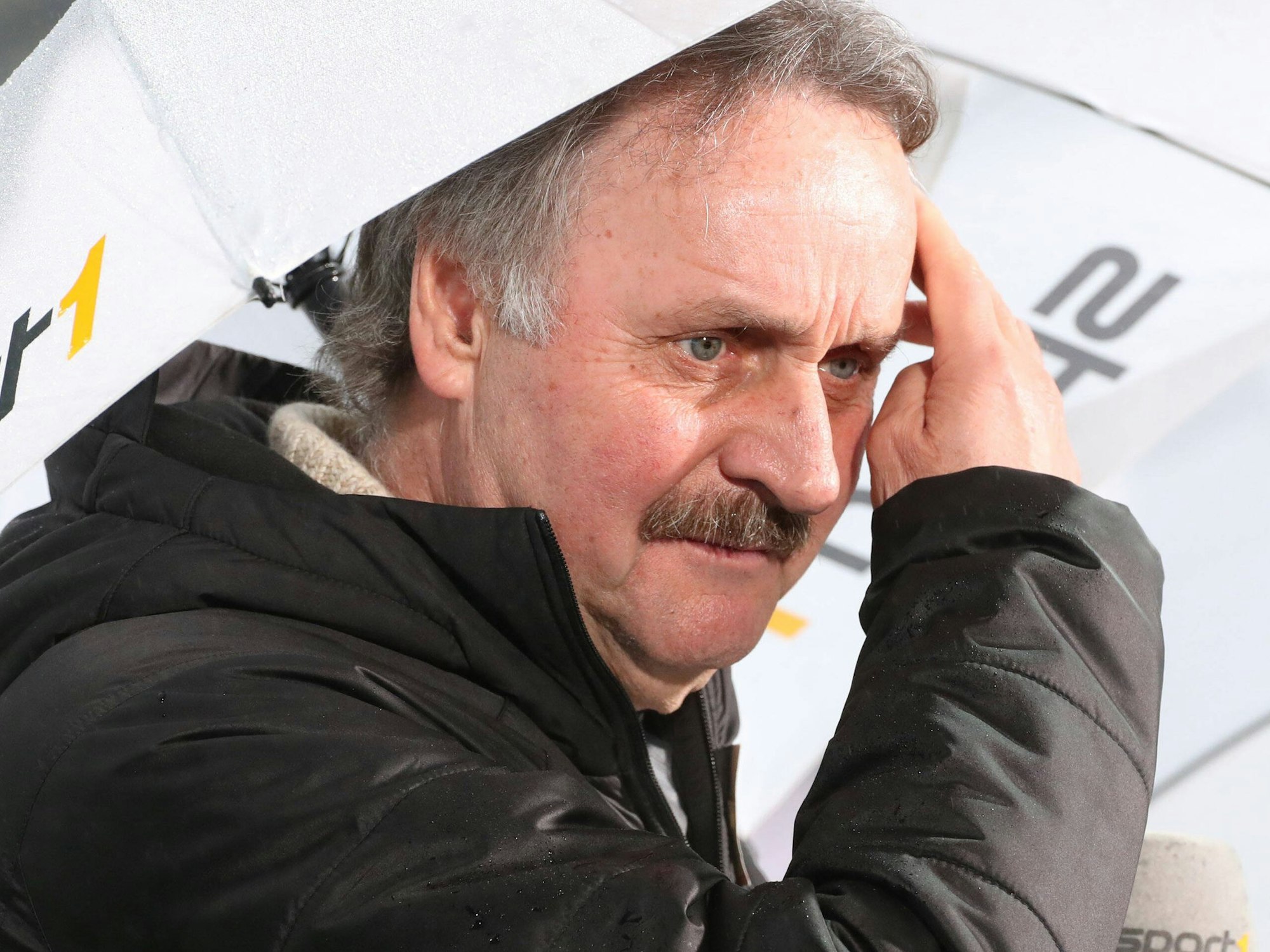 TV-Experte Peter Neururer mit Regenschirm im Stadion.
