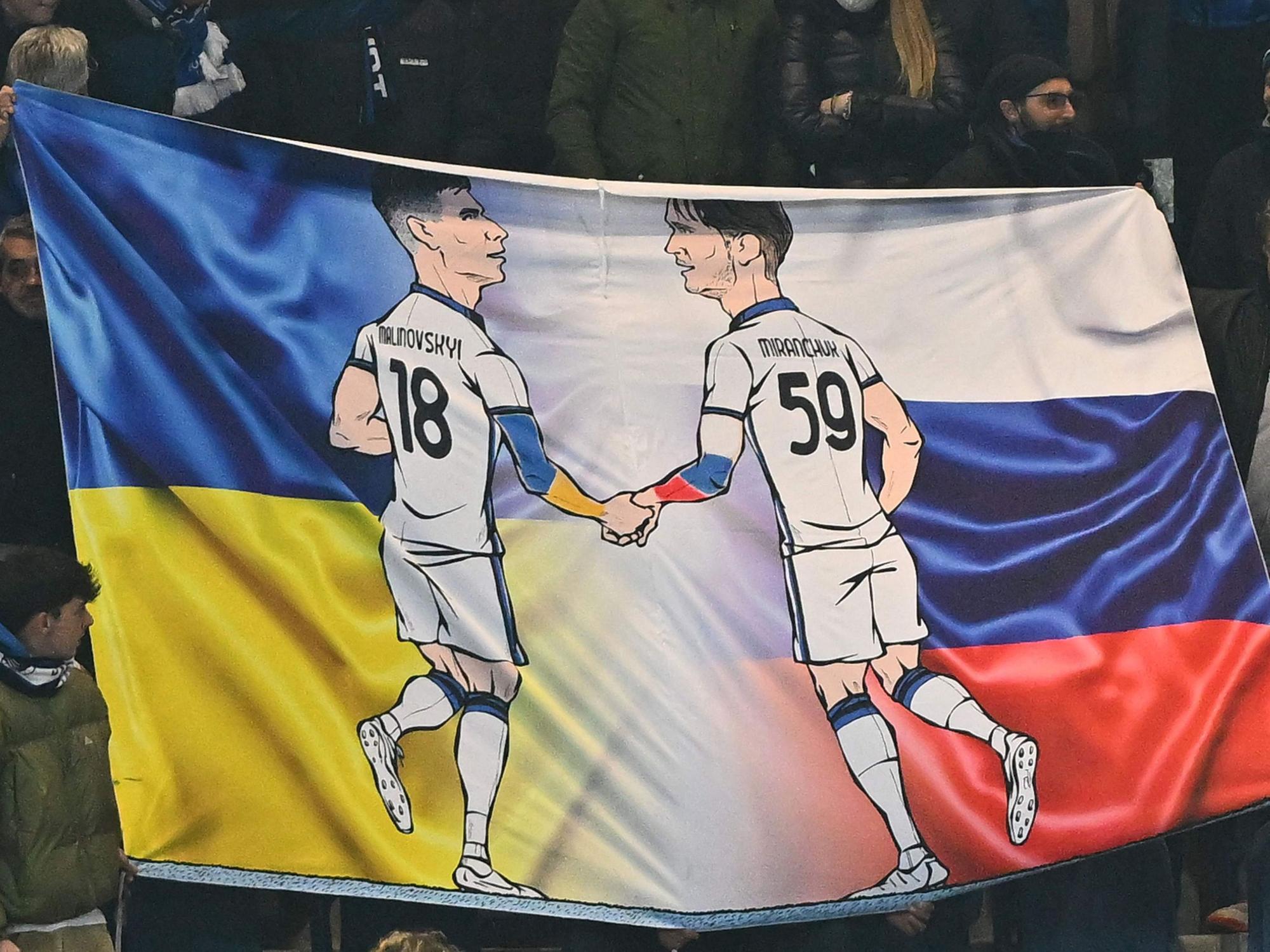 Zeichnungen der Atalanta-Profis Ruslan Malinowskyi und Alexej Mirantschuk beim Europa-League-Spiel zwischen Bergamo und Bayer Leverkusen. Im Hintergrund des Banners sind die Landesflaggen der Ukraine und Russlands zu sehen.
