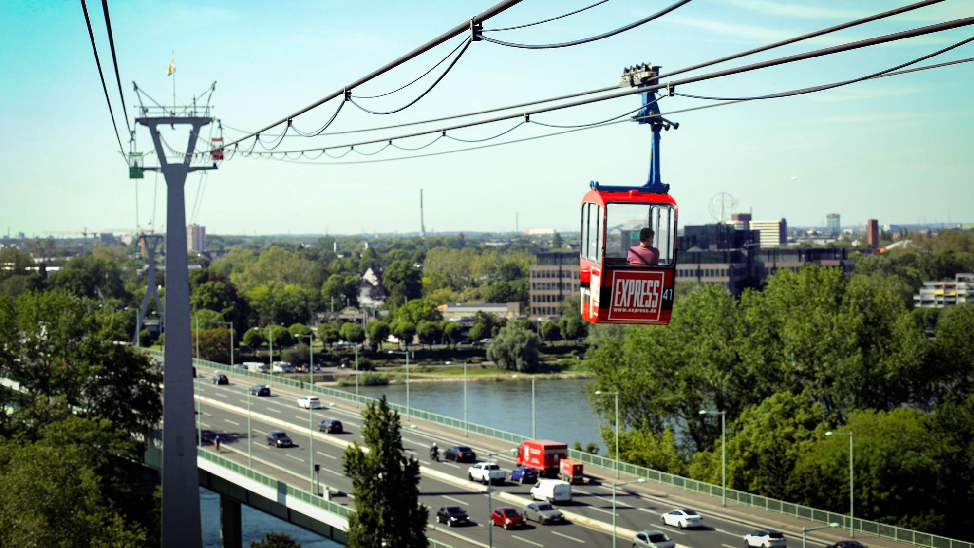 Gondel der Kölner Seilbahn mit EXPRESS-Logo fährt über die Stadt.
