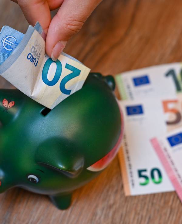 Ein Mädchen steckt einen 20-Euro-Schein in ein Sparschwein.