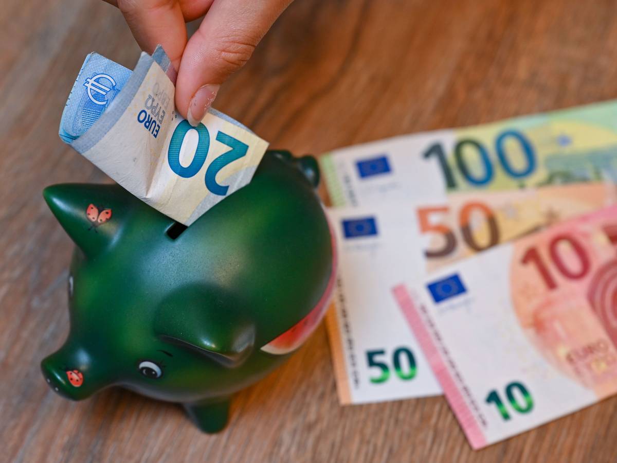Ein Mädchen steckt einen 20-Euro-Schein in ein Sparschwein.