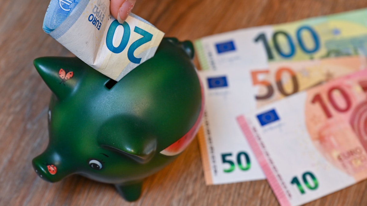 Ein Mädchen steckt einen 20-Euro-Schein in ein Sparschwein.